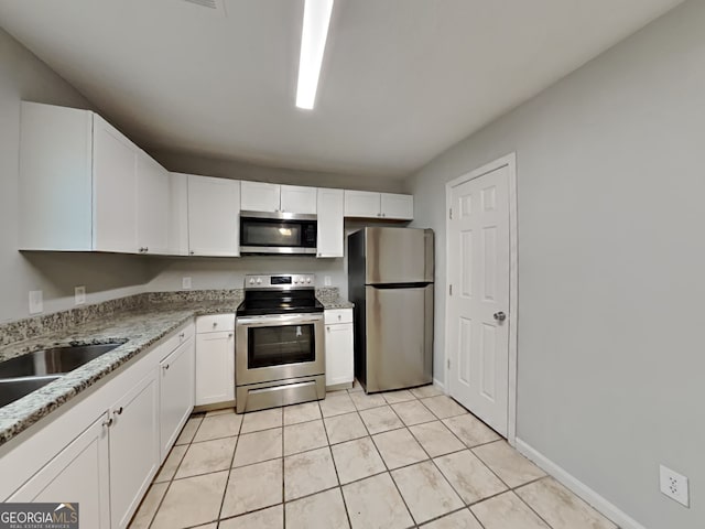 kitchen with light tile patterned flooring, appliances with stainless steel finishes, white cabinetry, sink, and light stone counters