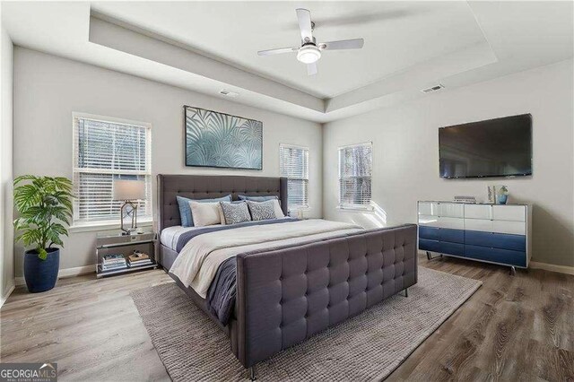 bedroom with ceiling fan, a raised ceiling, hardwood / wood-style floors, and multiple windows