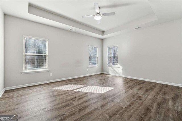 spare room with ceiling fan, dark hardwood / wood-style flooring, and a tray ceiling