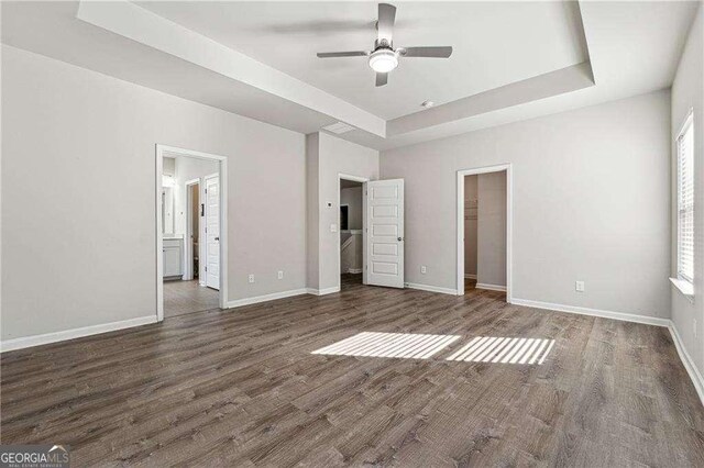 unfurnished bedroom with dark hardwood / wood-style floors, ensuite bathroom, a raised ceiling, a walk in closet, and a closet