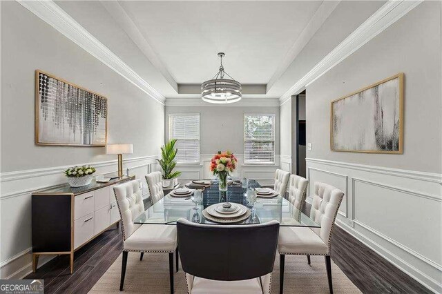 dining area featuring a notable chandelier, wood-type flooring, ornamental molding, and a raised ceiling