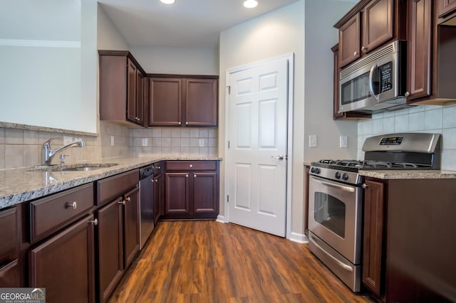 kitchen with appliances with stainless steel finishes, dark hardwood / wood-style floors, sink, backsplash, and light stone counters