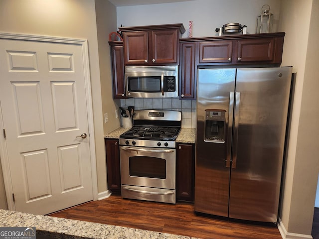 kitchen featuring appliances with stainless steel finishes, tasteful backsplash, dark brown cabinetry, light stone countertops, and dark wood-type flooring