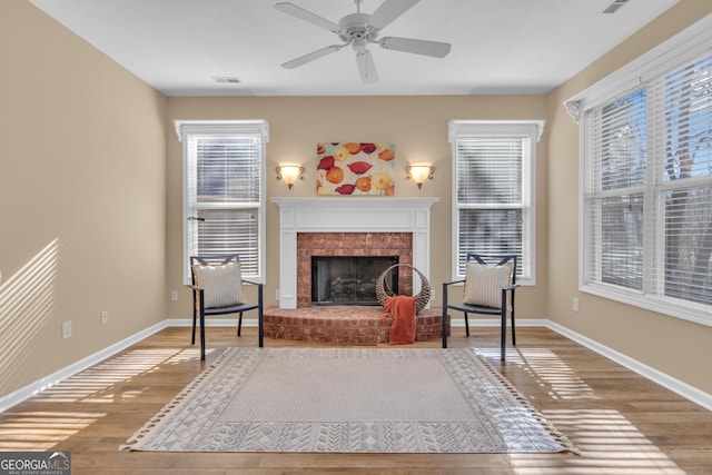 sitting room featuring visible vents, a brick fireplace, wood finished floors, and a healthy amount of sunlight