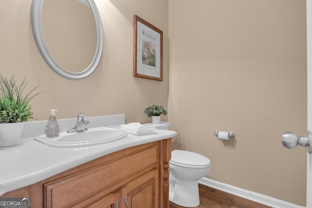 half bathroom featuring toilet, wood finished floors, vanity, and baseboards