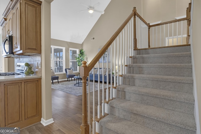 staircase featuring baseboards, visible vents, ceiling fan, high vaulted ceiling, and wood finished floors