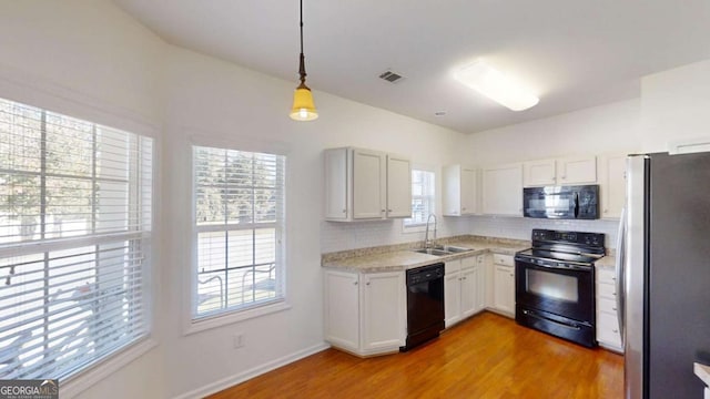 kitchen with white cabinetry, hanging light fixtures, black appliances, and sink