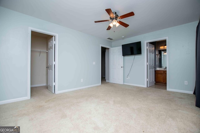 unfurnished bedroom with light carpet, ensuite bath, ceiling fan, and a spacious closet