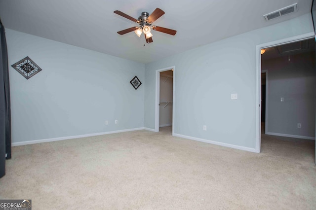 unfurnished bedroom with a walk in closet, light carpet, ceiling fan, and a closet