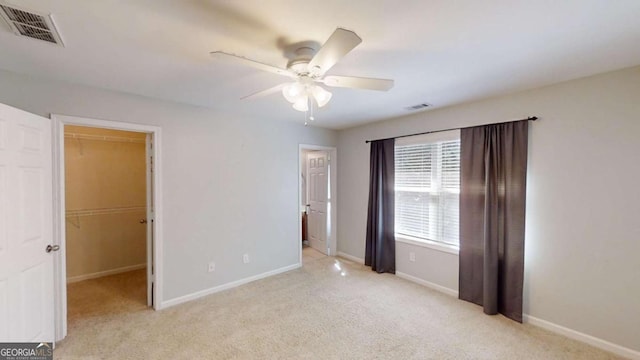 unfurnished bedroom featuring light carpet, a walk in closet, and ceiling fan