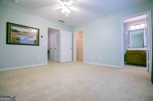 unfurnished bedroom featuring ceiling fan, ensuite bathroom, a walk in closet, light colored carpet, and a closet