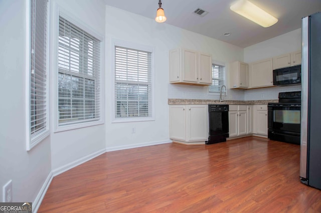 kitchen featuring decorative light fixtures, tasteful backsplash, white cabinetry, hardwood / wood-style flooring, and black appliances