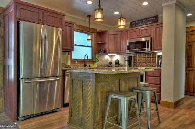 kitchen featuring decorative light fixtures, a kitchen island, stainless steel appliances, light stone countertops, and light hardwood / wood-style floors