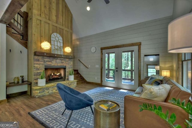 living room with hardwood / wood-style flooring, high vaulted ceiling, a stone fireplace, french doors, and wood walls