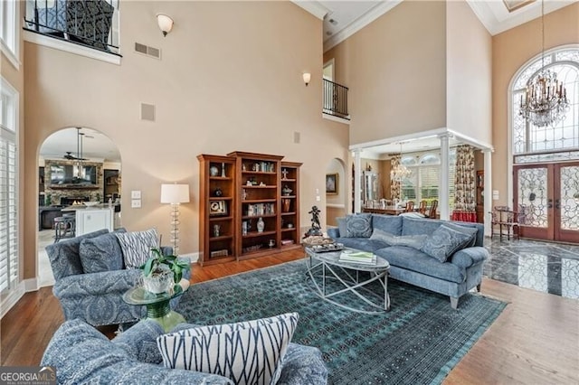 living room featuring hardwood / wood-style floors, a chandelier, a high ceiling, ornamental molding, and french doors