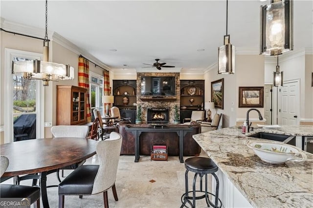 dining area featuring ceiling fan, a large fireplace, ornamental molding, and sink