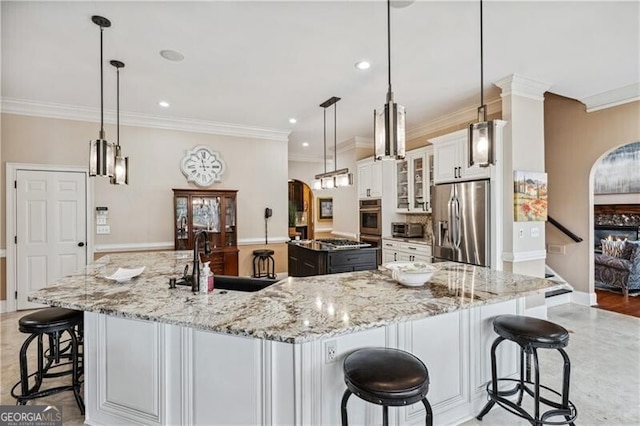 kitchen featuring sink, appliances with stainless steel finishes, white cabinetry, decorative light fixtures, and a large island with sink