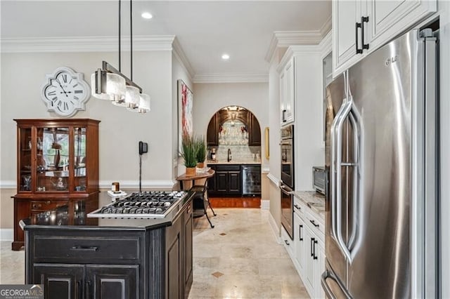 kitchen with appliances with stainless steel finishes, decorative light fixtures, tasteful backsplash, white cabinets, and ornamental molding