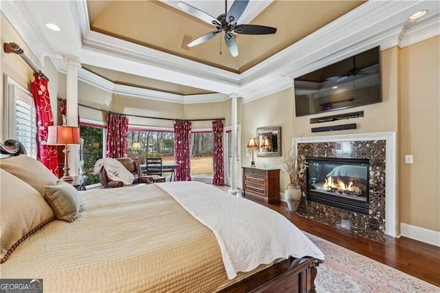 bedroom featuring dark hardwood / wood-style flooring, crown molding, a high end fireplace, and a raised ceiling