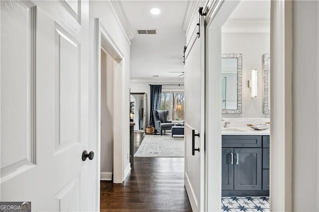 corridor featuring dark hardwood / wood-style floors, ornamental molding, a barn door, and sink