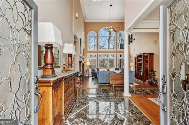 foyer featuring a towering ceiling, ornamental molding, ceiling fan, and ornate columns