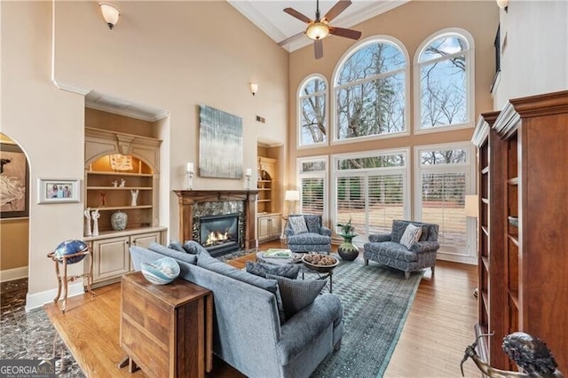 living room with crown molding, light hardwood / wood-style floors, a premium fireplace, and ceiling fan