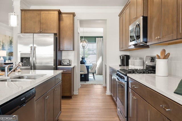 kitchen with sink, decorative light fixtures, ornamental molding, stainless steel appliances, and light stone countertops