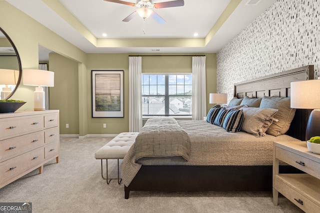 bedroom featuring light carpet, ceiling fan, and a tray ceiling