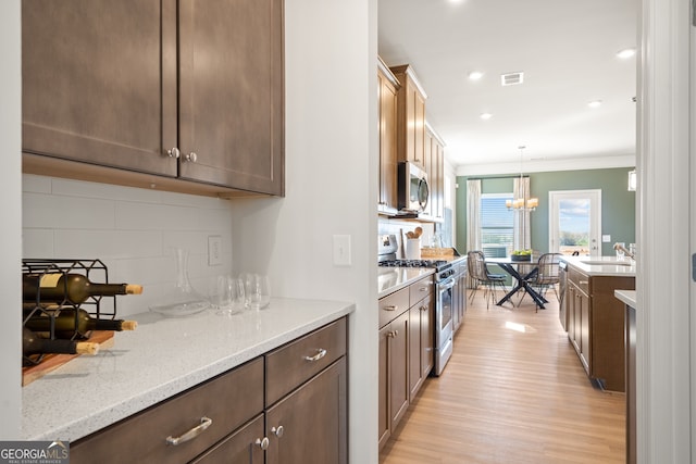 kitchen with decorative light fixtures, tasteful backsplash, stainless steel appliances, light stone countertops, and light hardwood / wood-style flooring