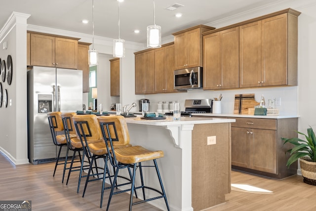 kitchen with decorative light fixtures, a kitchen bar, a kitchen island with sink, light hardwood / wood-style floors, and stainless steel appliances