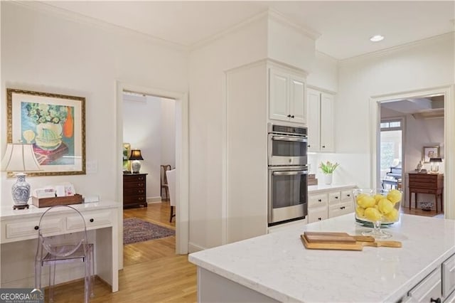 kitchen with white cabinetry, light stone countertops, ornamental molding, and stainless steel double oven