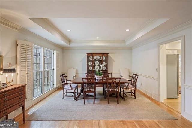 dining area featuring a raised ceiling, ornamental molding, and light hardwood / wood-style floors