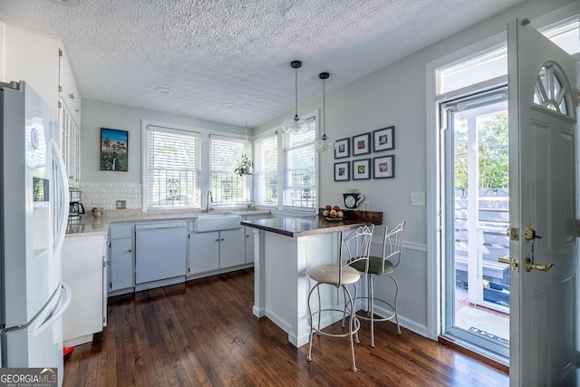 kitchen featuring pendant lighting, white cabinets, a kitchen bar, kitchen peninsula, and white appliances