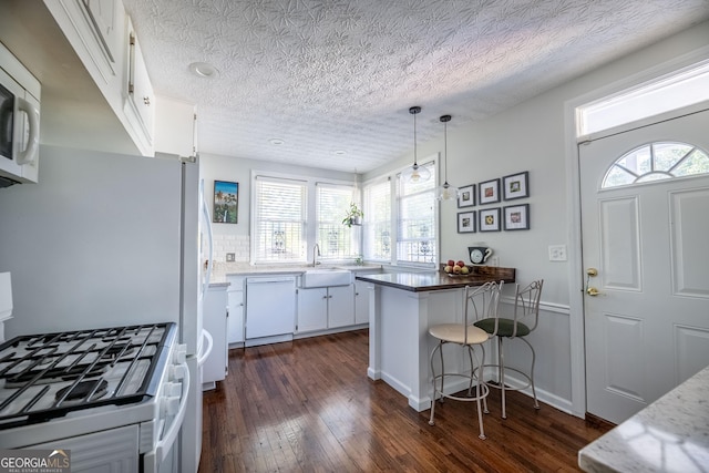 kitchen featuring pendant lighting, sink, white appliances, white cabinets, and a kitchen bar