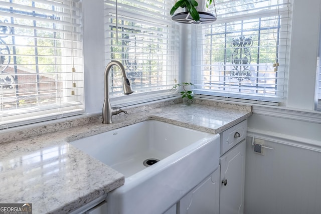 interior space featuring light stone counters, sink, a wealth of natural light, and white cabinets