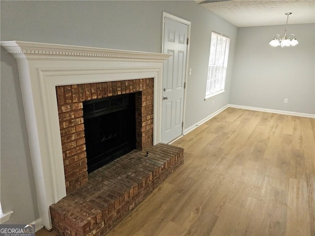 living room featuring an inviting chandelier, a fireplace, a textured ceiling, and light wood-type flooring