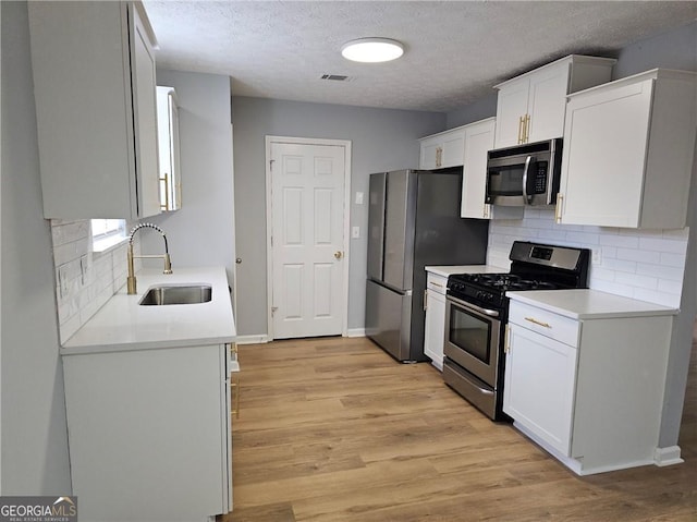 kitchen with sink, white cabinetry, light wood-type flooring, appliances with stainless steel finishes, and decorative backsplash