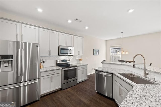 kitchen featuring light stone counters, appliances with stainless steel finishes, sink, and hanging light fixtures