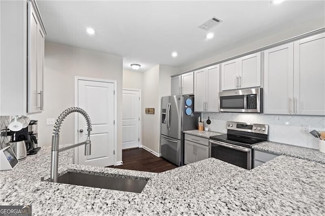 kitchen featuring sink, dark hardwood / wood-style flooring, decorative backsplash, stainless steel appliances, and light stone countertops