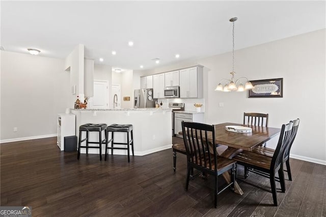 dining area featuring dark wood-type flooring, sink, and an inviting chandelier