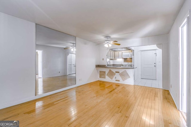 unfurnished living room with sink, ceiling fan, and light hardwood / wood-style flooring