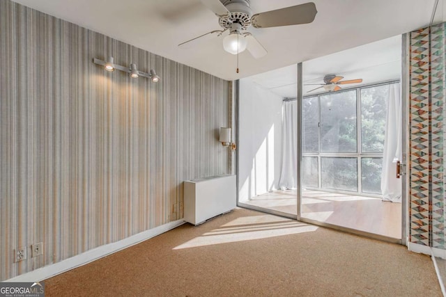 carpeted empty room with ceiling fan, a wall of windows, and plenty of natural light