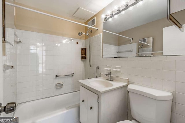 full bathroom with vanity, toilet, tiled shower / bath combo, and tile walls