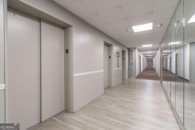 hallway featuring a paneled ceiling, elevator, and light wood-type flooring