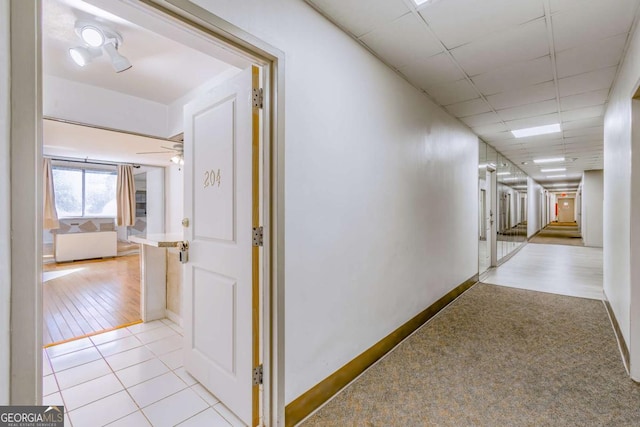 hallway featuring light tile patterned flooring and a paneled ceiling