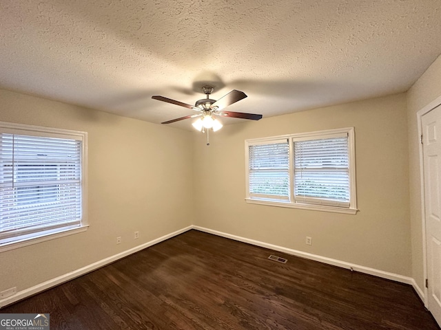 spare room featuring ceiling fan, a healthy amount of sunlight, dark hardwood / wood-style floors, and a textured ceiling