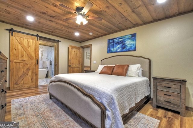 bedroom featuring ensuite bath, light hardwood / wood-style flooring, wooden ceiling, and a barn door