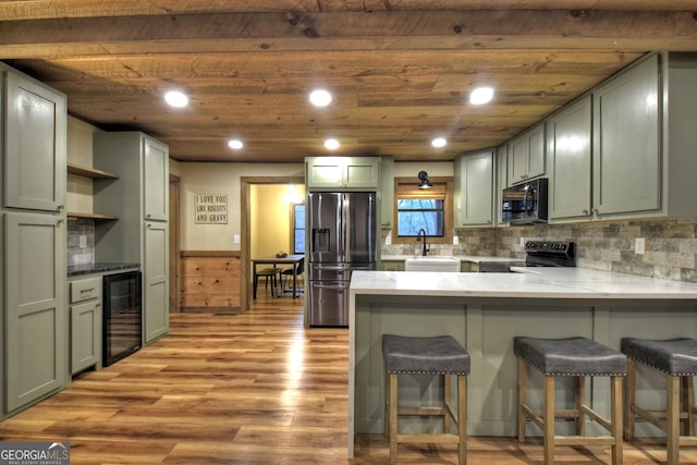 kitchen with a kitchen breakfast bar, wine cooler, black appliances, kitchen peninsula, and light wood-type flooring