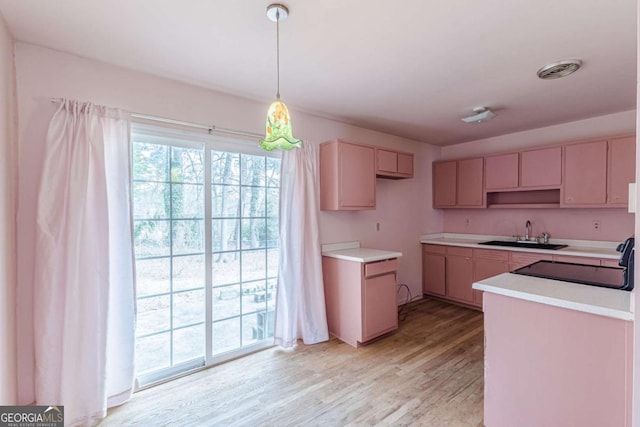 kitchen featuring stove, sink, light hardwood / wood-style floors, and decorative light fixtures