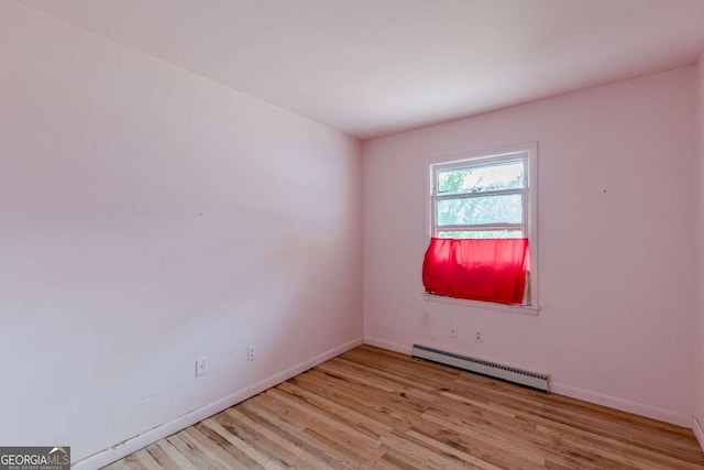 spare room featuring a baseboard heating unit and light wood-type flooring